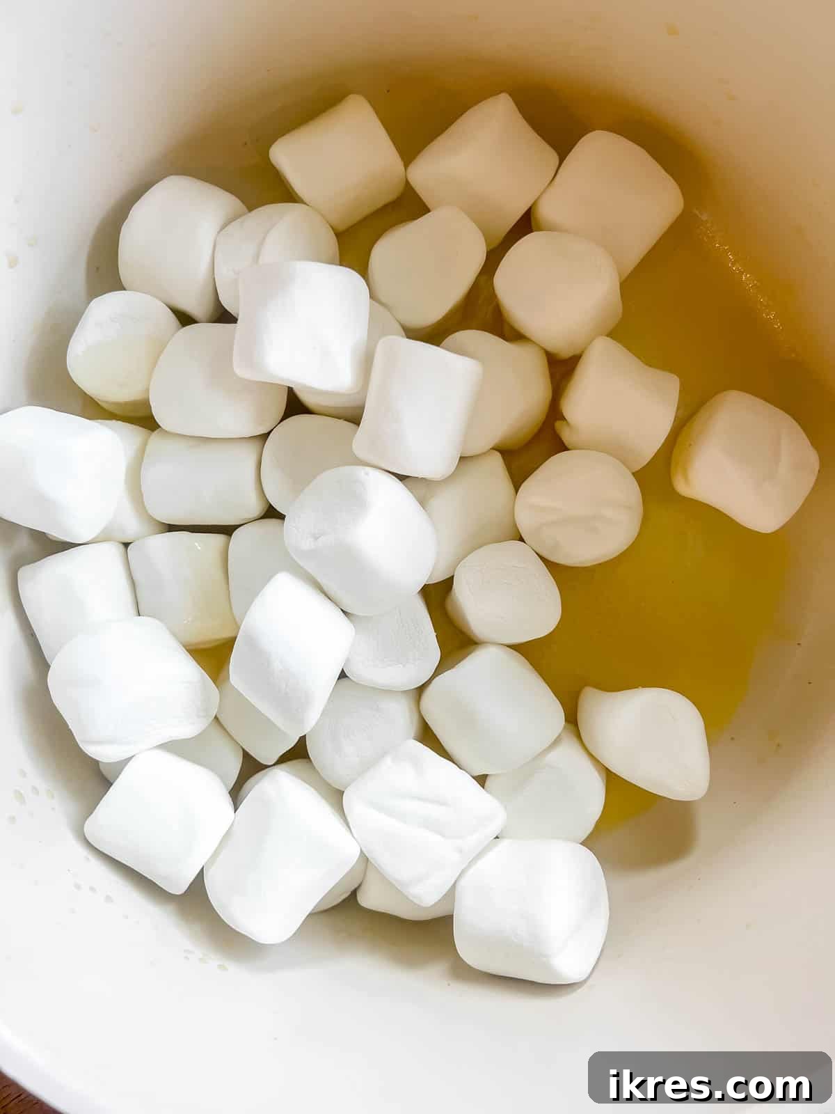Fluffy marshmallows being added to the saucepan with melted butter, ready to be transformed into a gooey base.