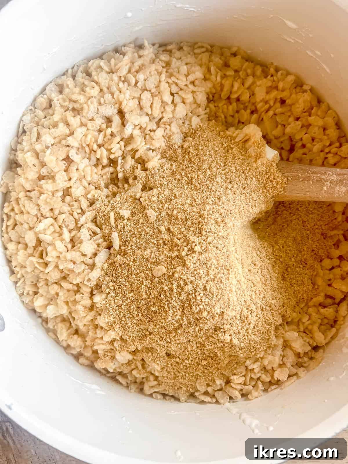 Crispy rice cereal and 1 cup of ground graham crackers are added to the warm, melted marshmallow mixture in the saucepan.