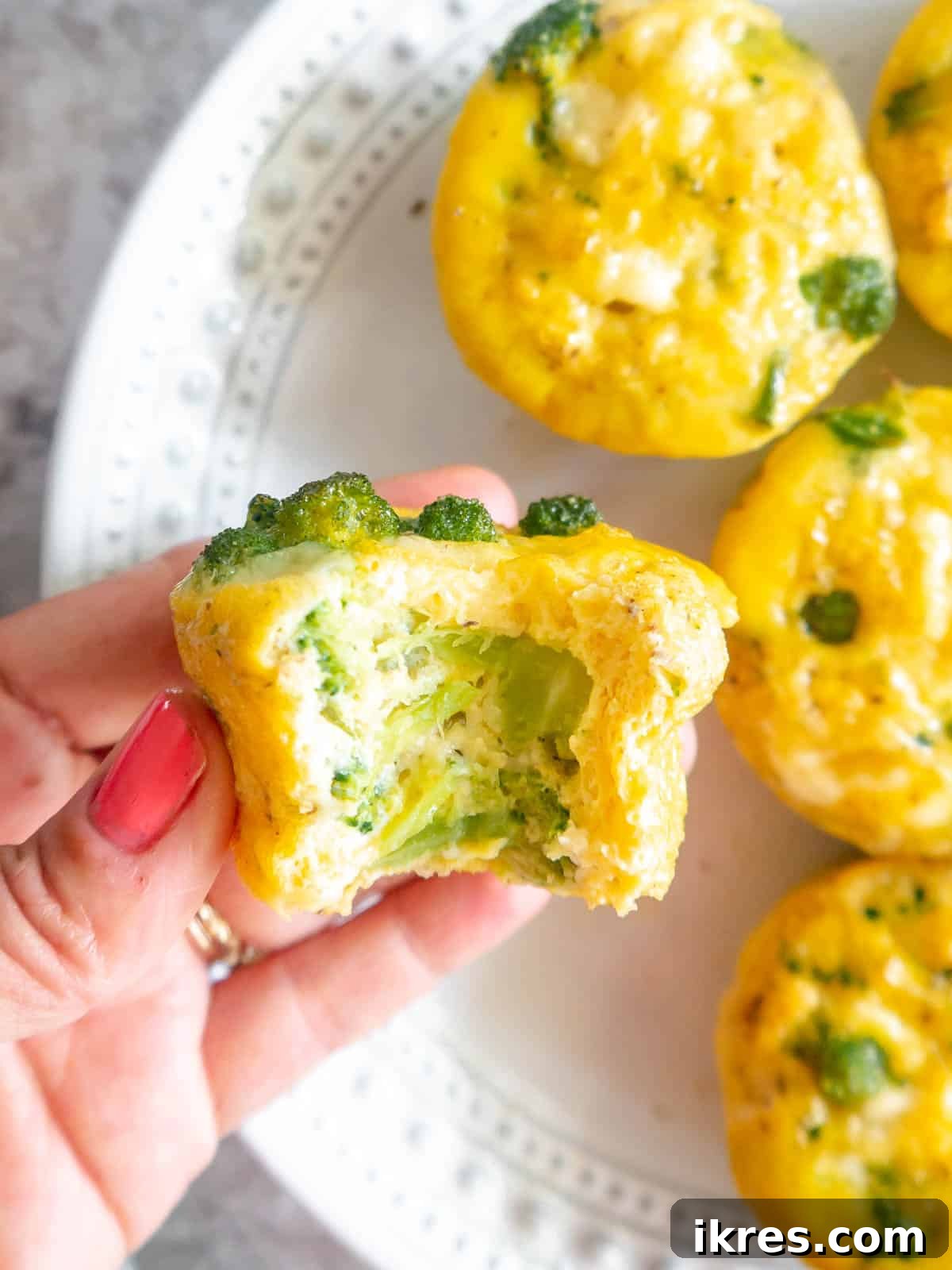 A bite taken out of a fluffy broccoli cheddar egg bite, showing the cheesy, veggie-filled interior.