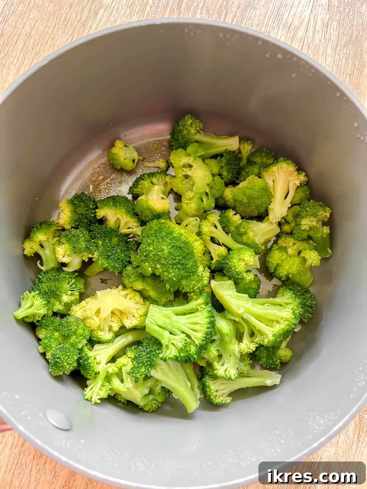 Fresh broccoli florets steaming in a covered pan on the stove.