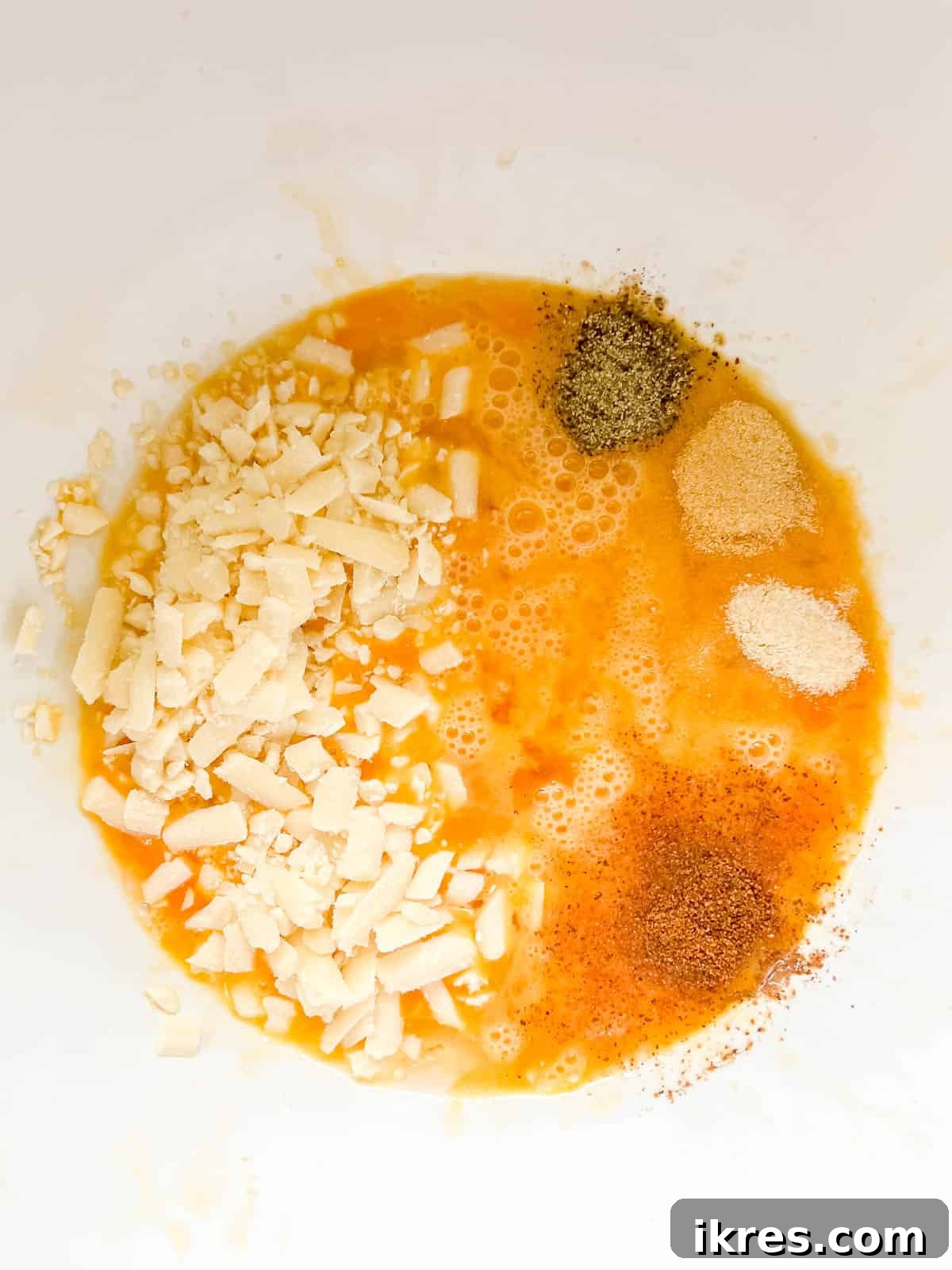 Shredded cheddar cheese, onion powder, garlic powder, salt, pepper, and ground nutmeg added to the whisked eggs in a bowl.