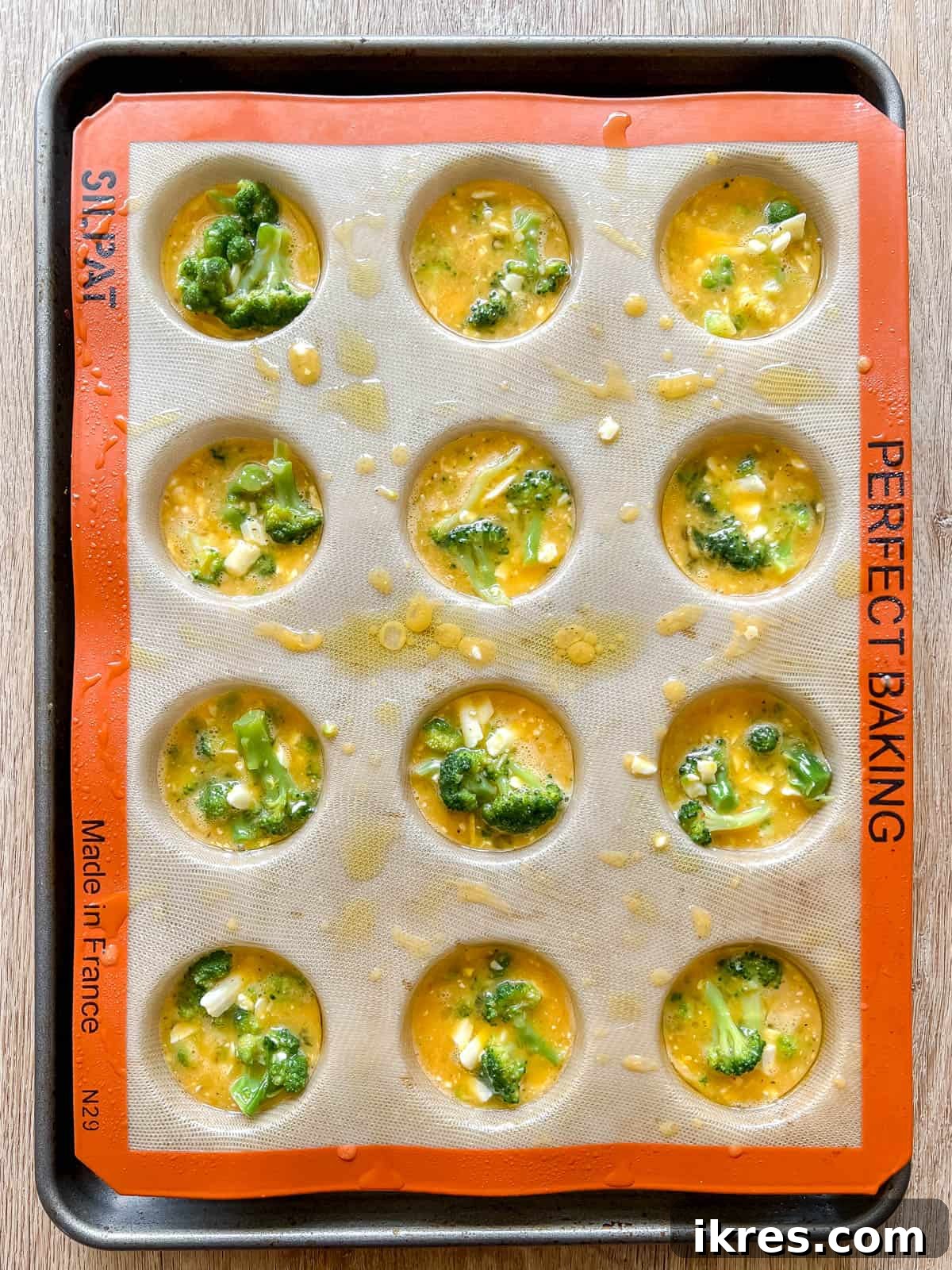 The broccoli egg mixture being poured into individual compartments of a muffin tin.