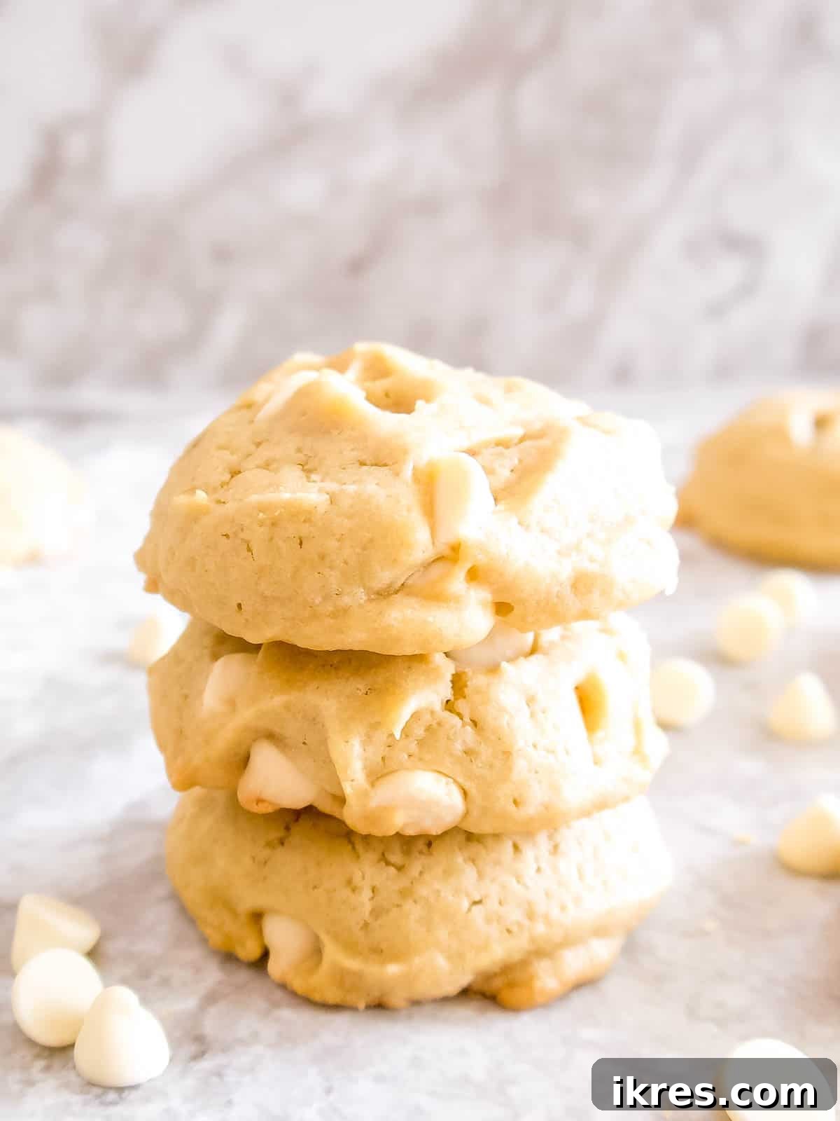 A tempting stack of three warm, freshly baked white chocolate chip cookies, highlighting their soft texture and abundance of gooey white chocolate.