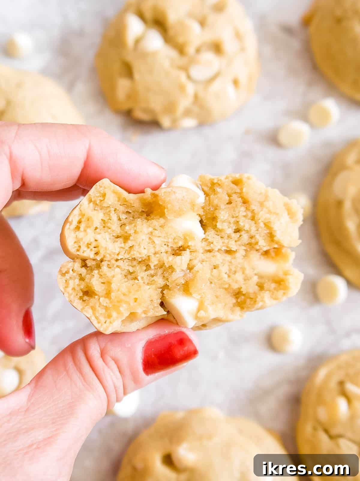 A close-up view of a perfectly baked white chocolate chip cookie, cut in half to reveal its soft, chewy interior studded with melted white chocolate chips.