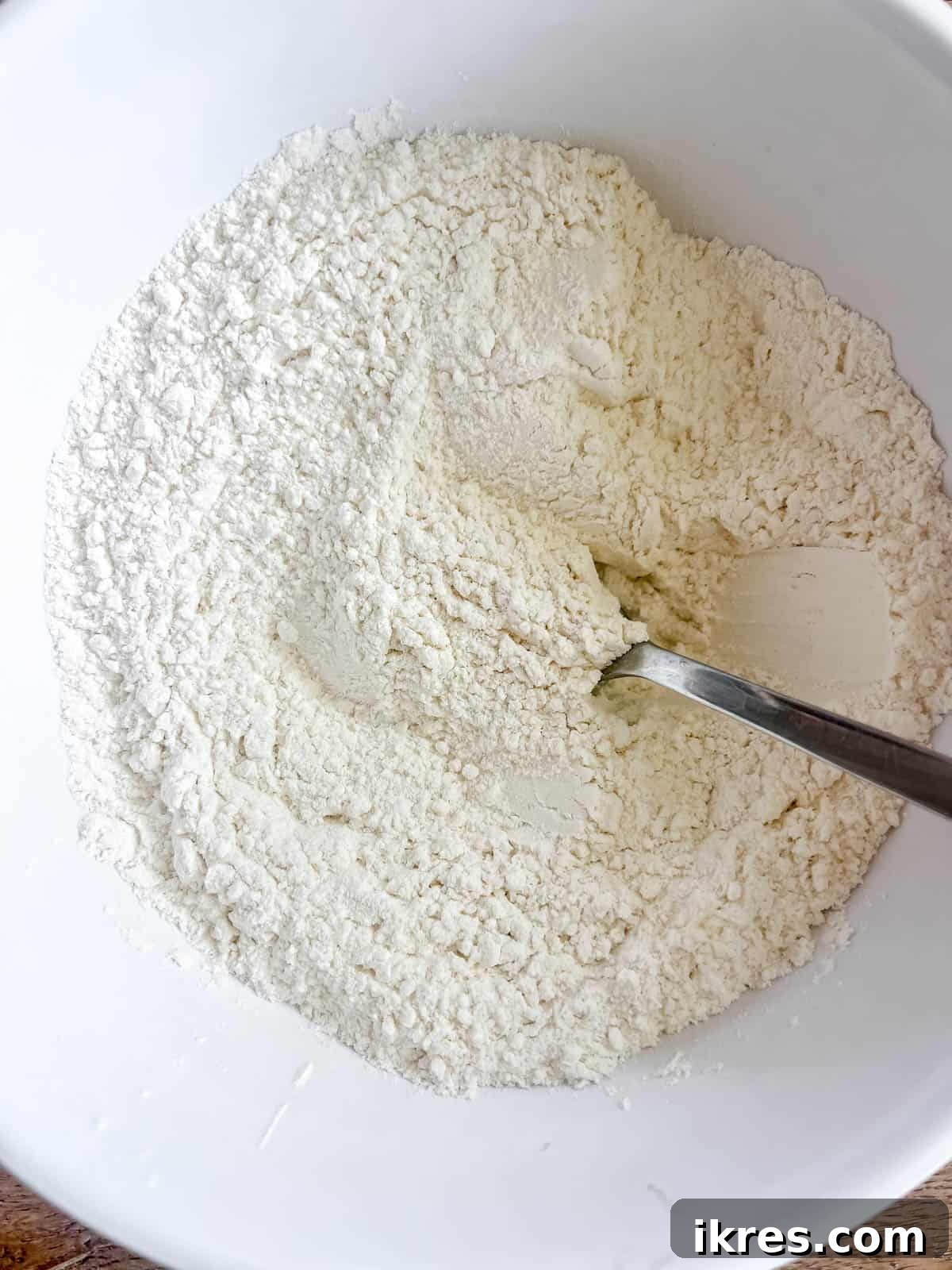 A white bowl containing dry ingredients for cookies: all-purpose flour, baking soda, and a pinch of salt, pre-mixed and ready.