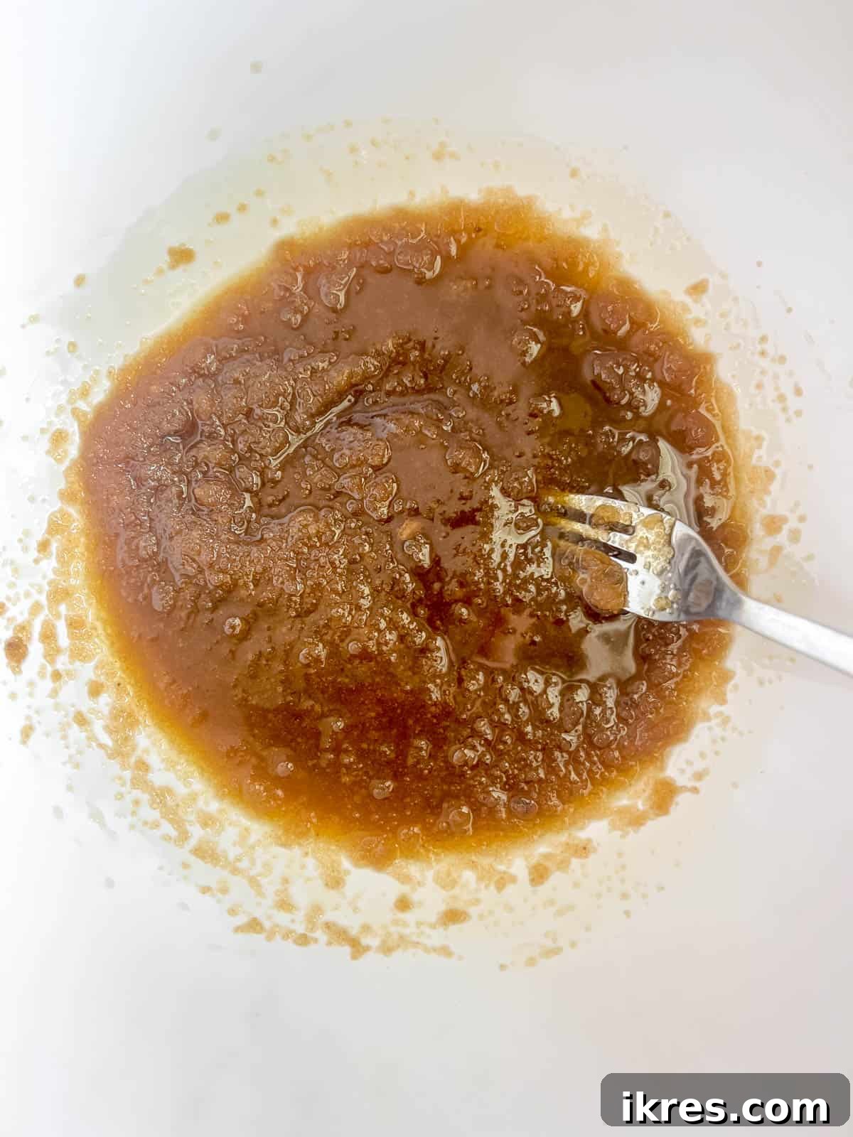 A bowl showing a smooth mixture of rich brown sugar thoroughly combined with olive oil, forming the wet base for the cookie dough.