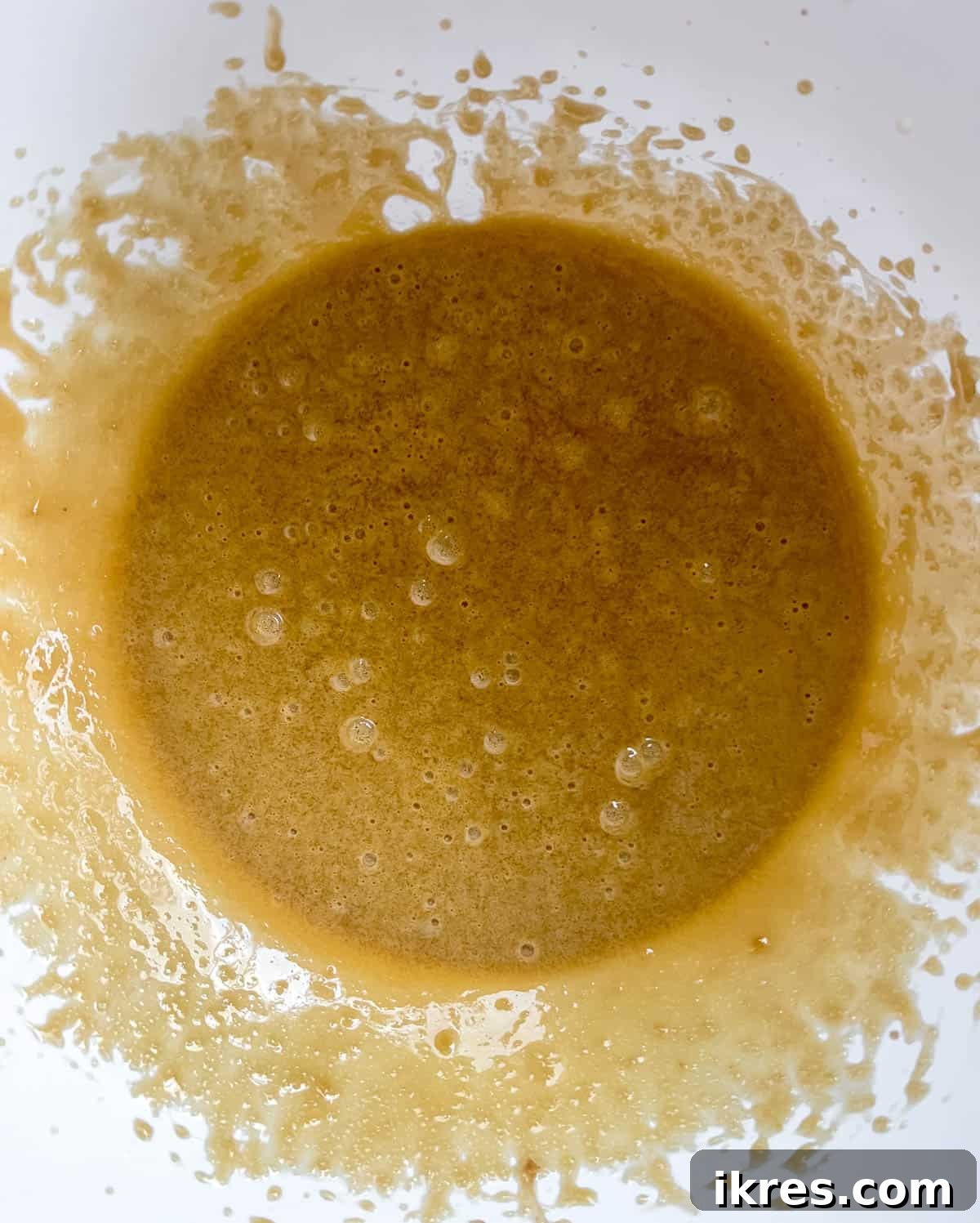 A mixing bowl filled with the whisked wet ingredients: olive oil, brown sugar, eggs, and vanilla extract, creating a creamy, aromatic base.
