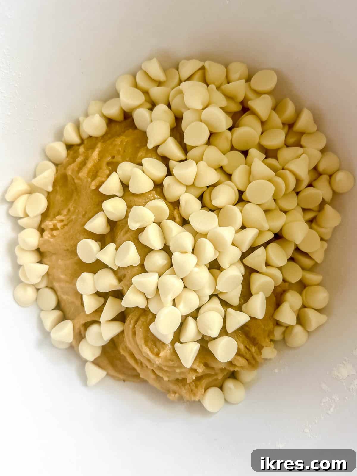 Freshly prepared cookie dough, studded with a generous amount of white chocolate chips, ready for its final mix before scooping.