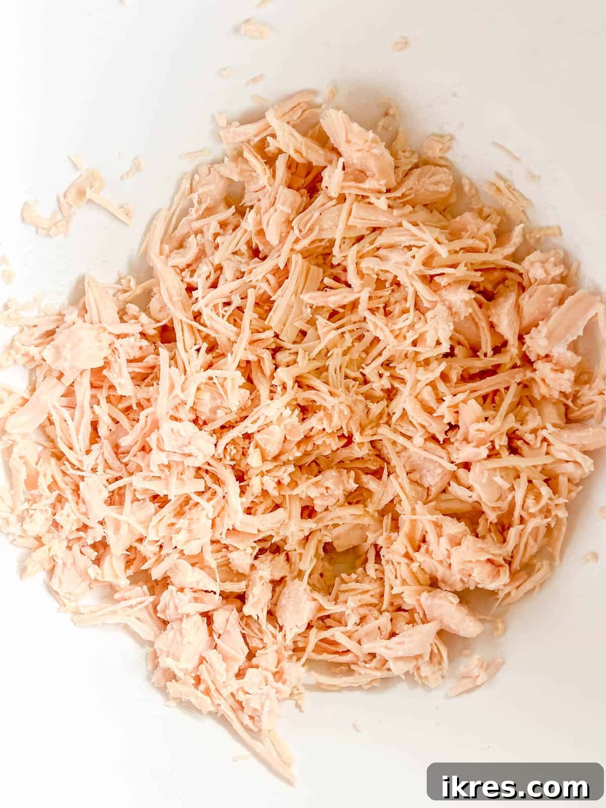 Drained canned chicken breast shredded in a mixing bowl.