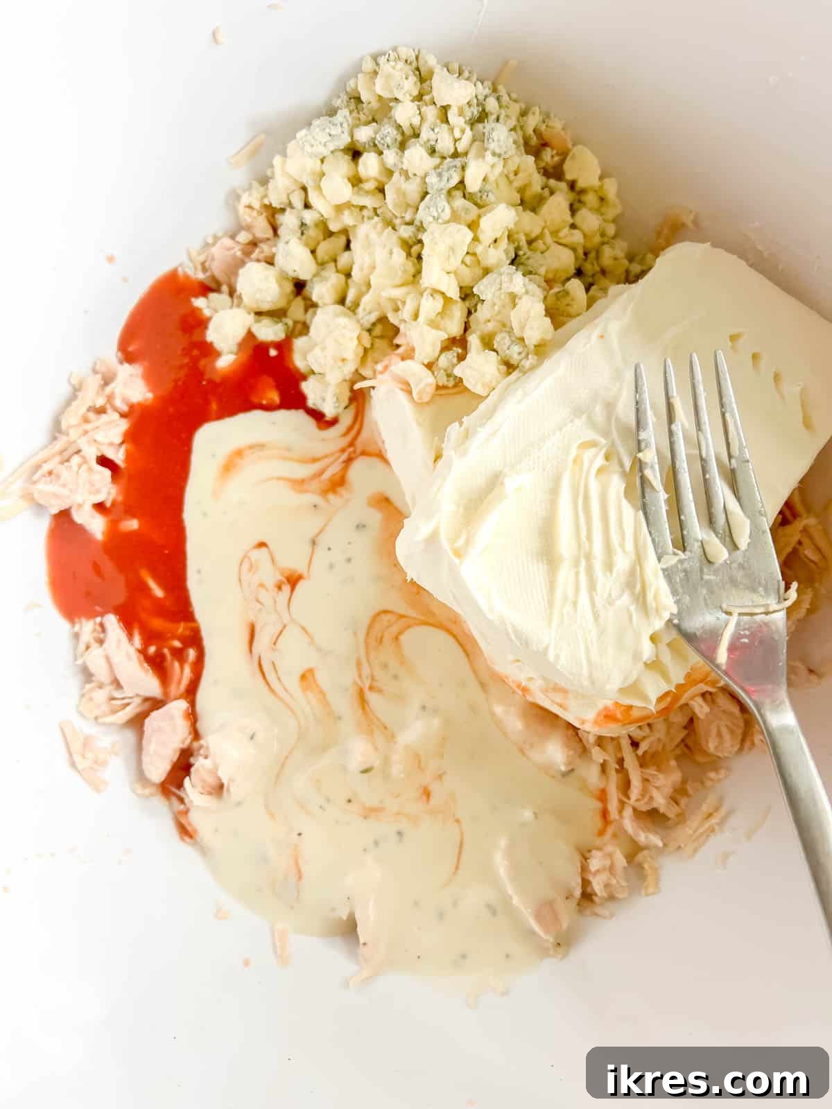 All buffalo chicken dip ingredients (hot sauce, ranch, softened cream cheese, blue cheese, and half of the cheddar) added to the shredded chicken in a bowl.