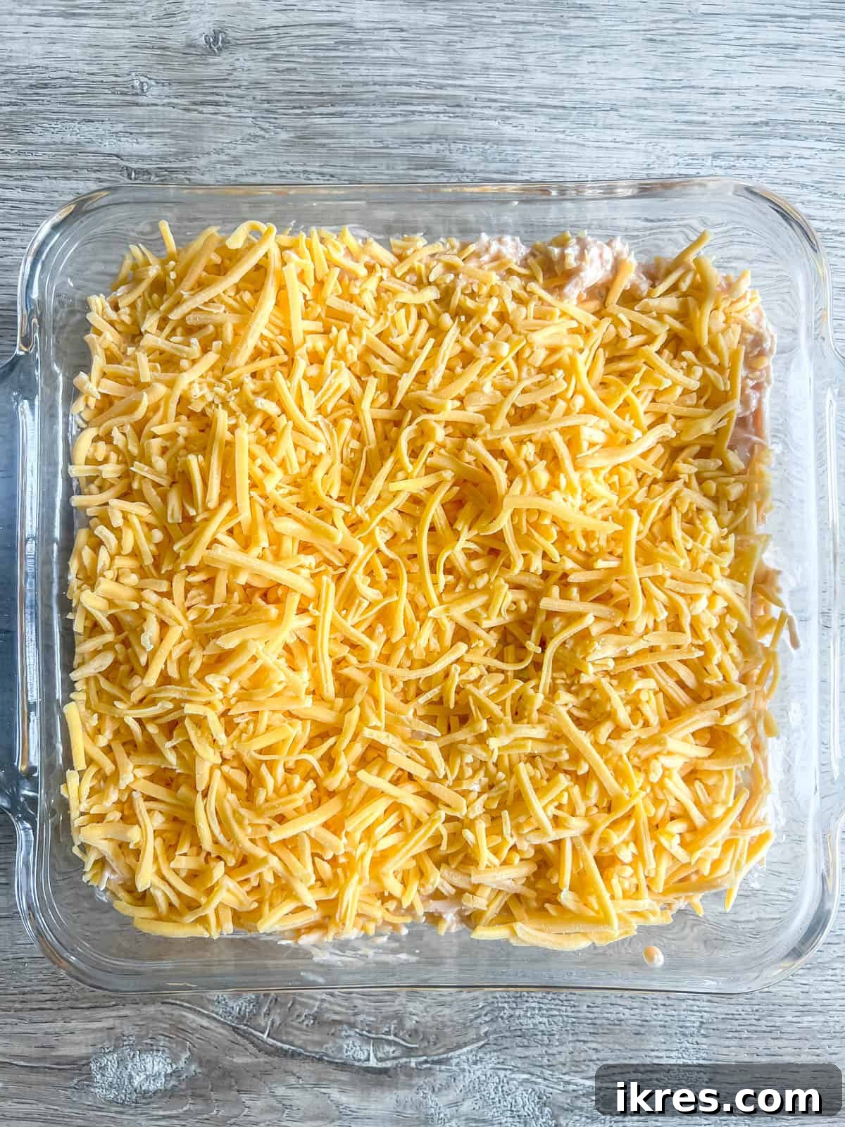 Buffalo chicken dip mixture spread evenly in an 8x8 inch baking dish, topped with the remaining shredded cheddar cheese, before baking.