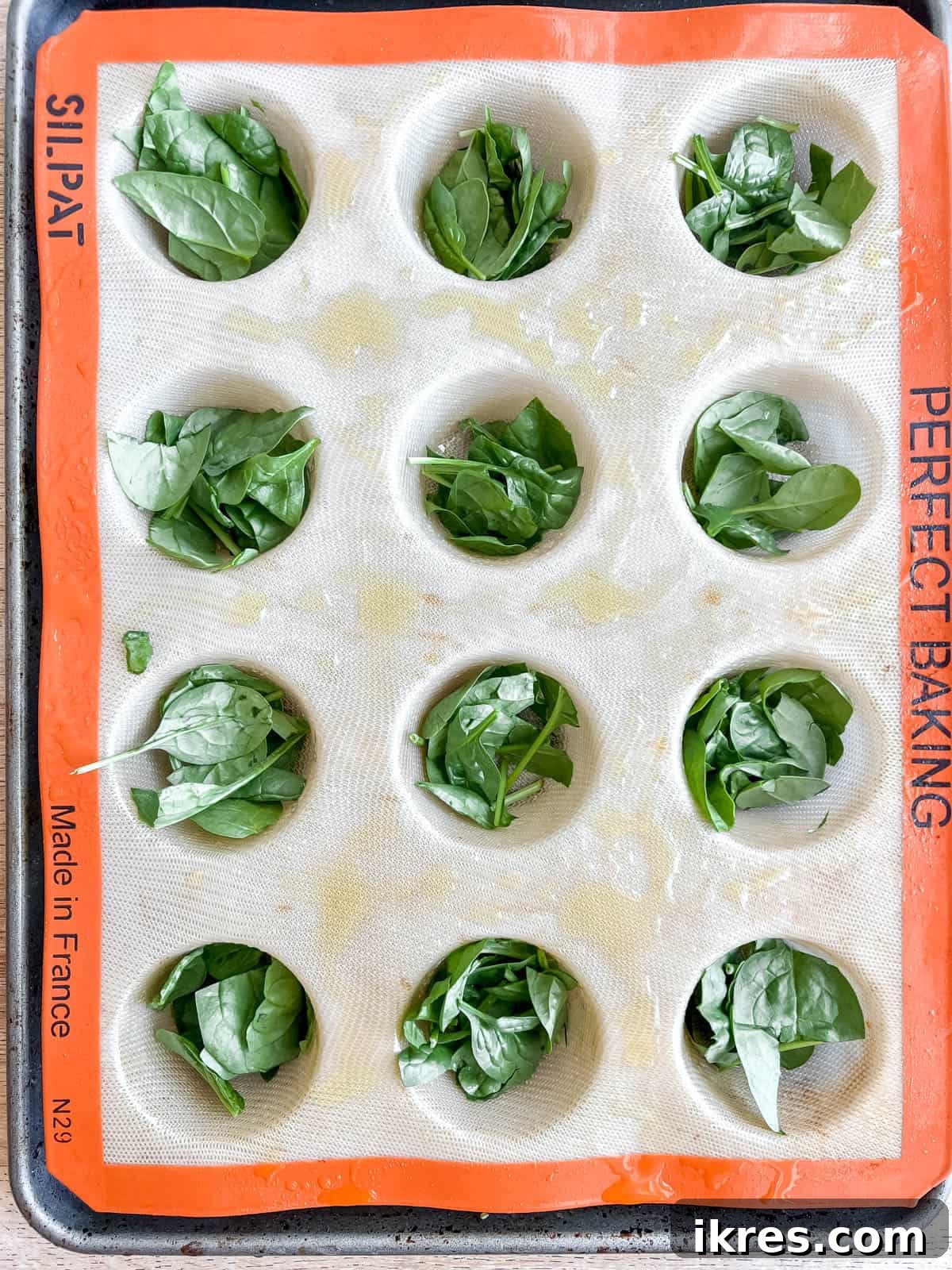 Mediterranean Spinach Feta Egg Muffins 7 Chopped fresh spinach evenly distributed into each compartment of a muffin tin.