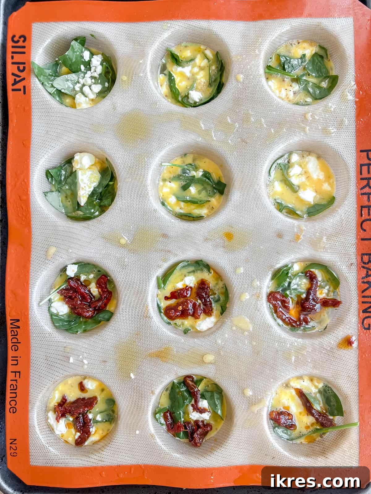 Mediterranean Spinach Feta Egg Muffins 8 Egg mixture being poured over the spinach in each muffin tin, with additional feta sprinkled on top.