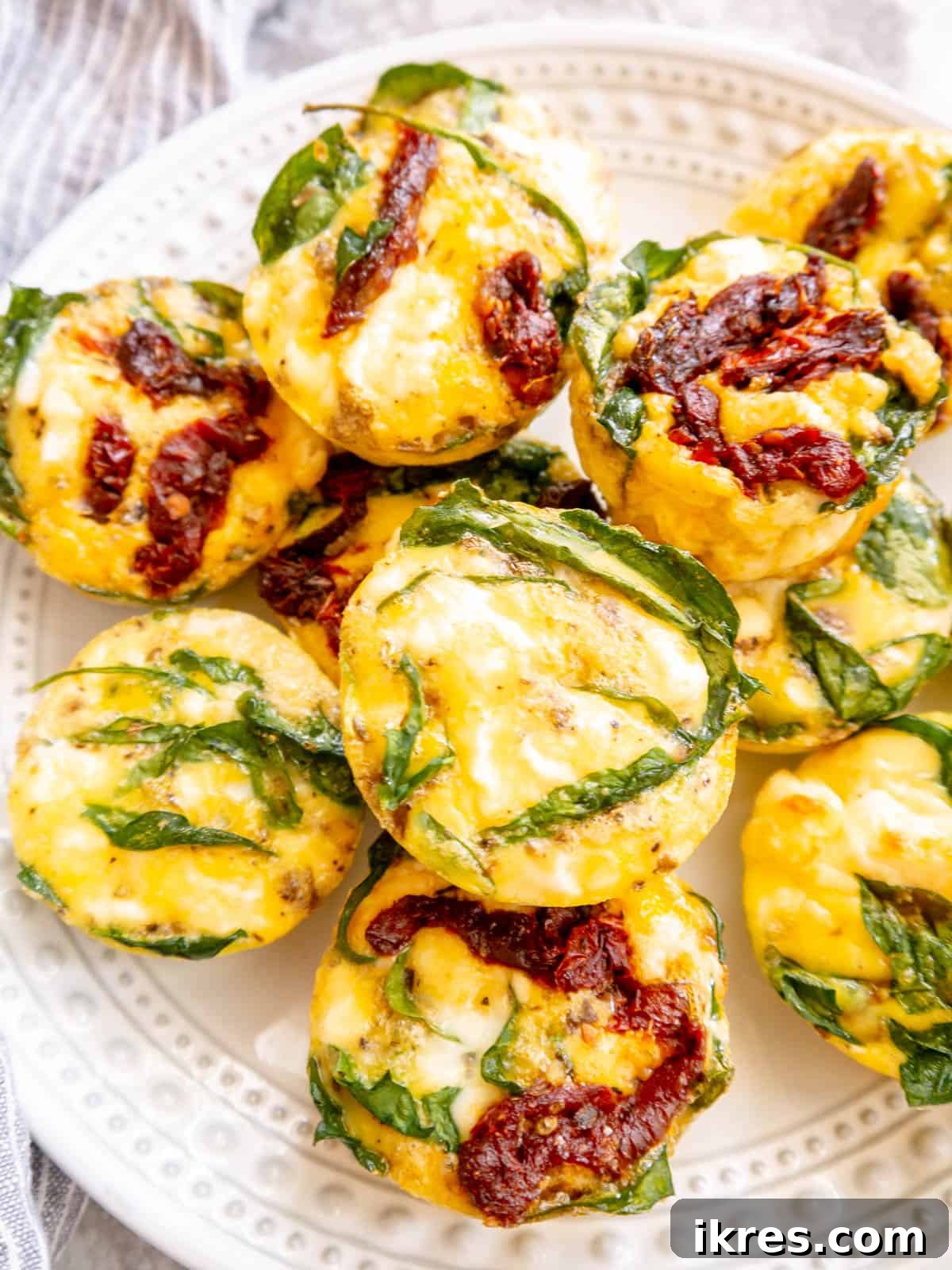 Mediterranean Spinach Feta Egg Muffins 10 Several spinach egg bites arranged on a white plate, garnished with fresh herbs, ready for a healthy meal.