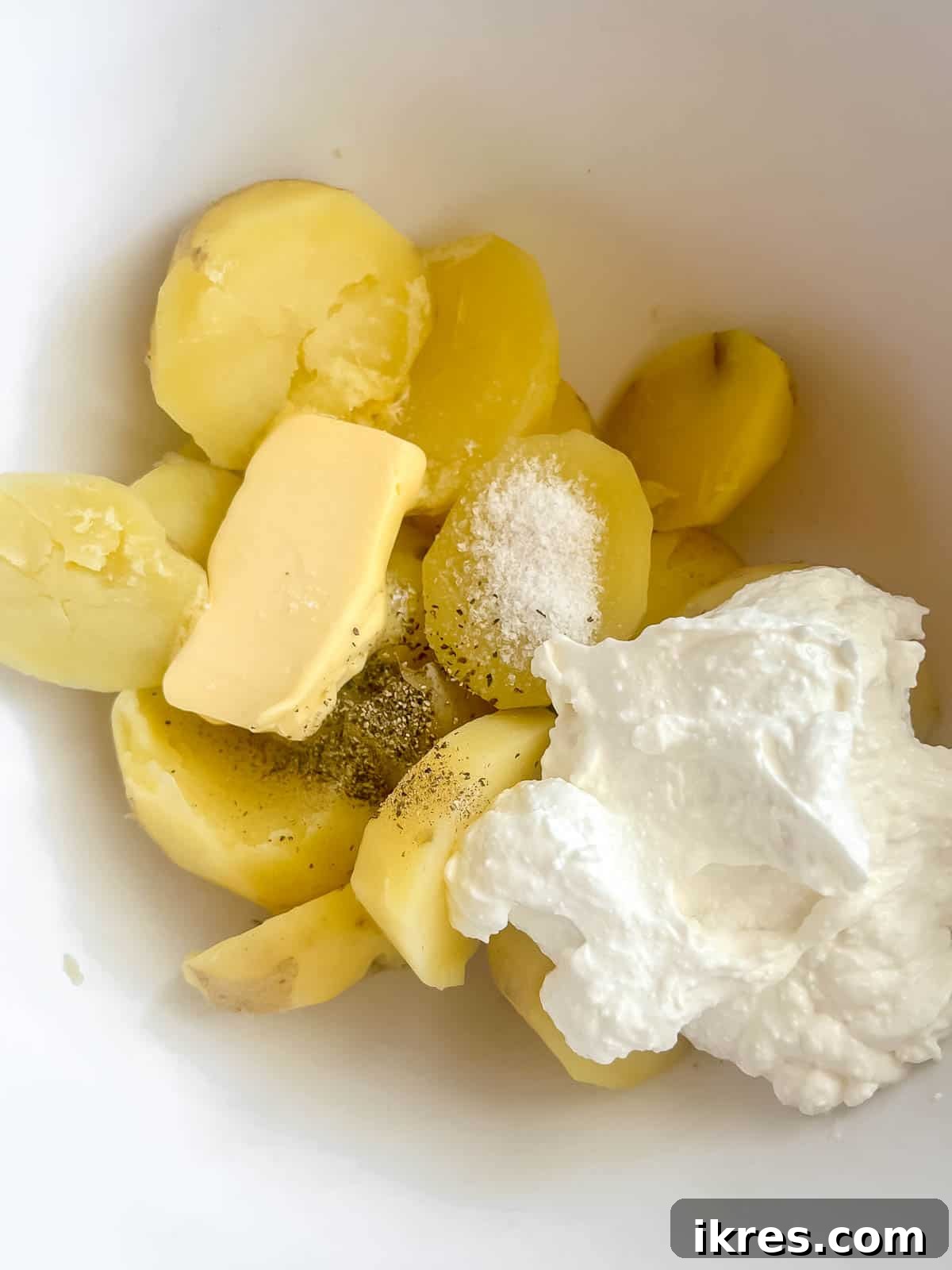 Whipped Cottage Cheese Potatoes 6 Hot, boiled potatoes, whipped cottage cheese, pats of butter, and seasonings gathered in a large mixing bowl, ready to be mashed.