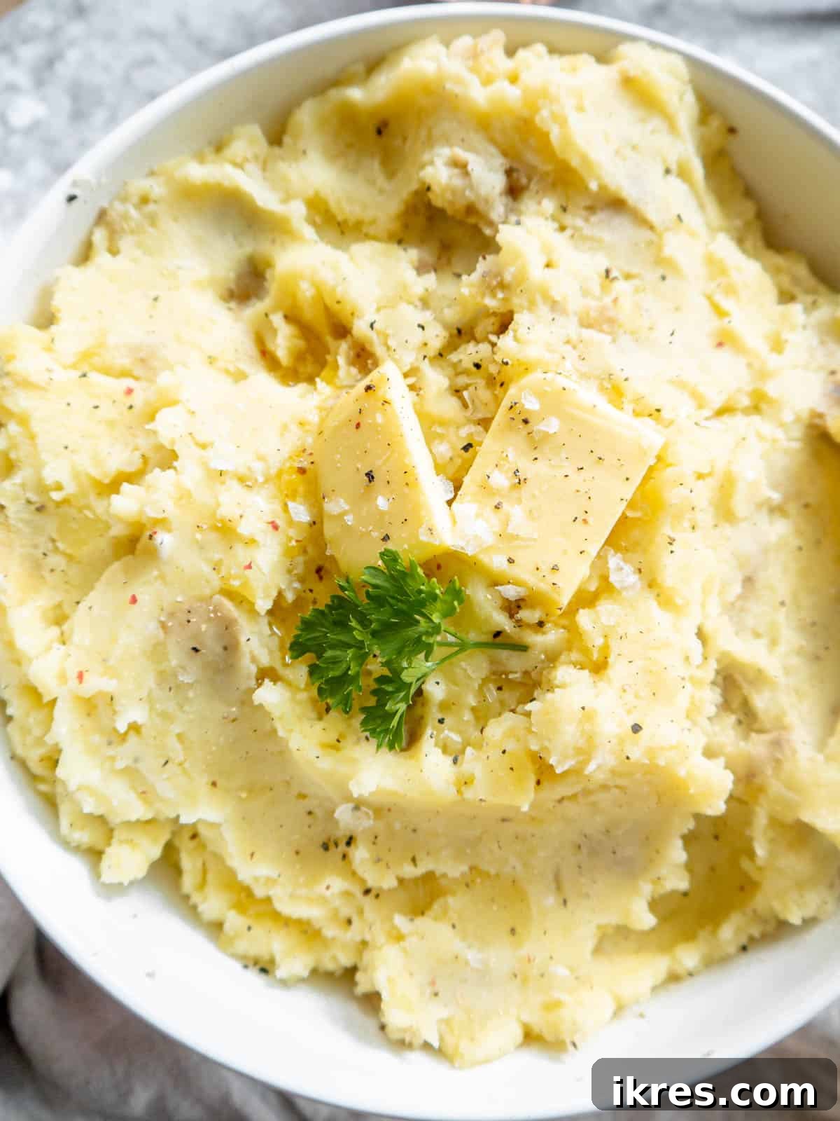 Whipped Cottage Cheese Potatoes 8 A close-up shot of a serving of cottage cheese mashed potatoes in a rustic bowl, with a pat of butter melting on top, garnished with a sprinkle of fresh herbs.