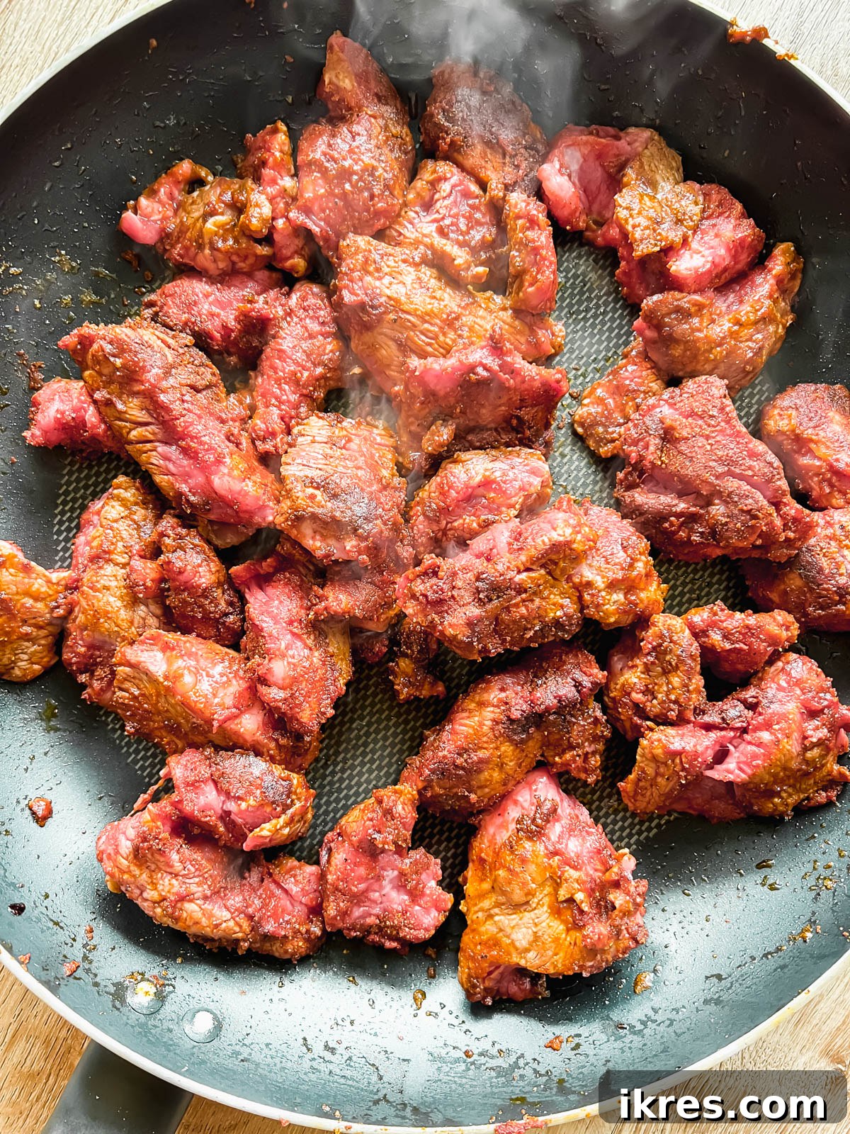Seared beef stew meat with tomato paste and spices in a hot frying pan.