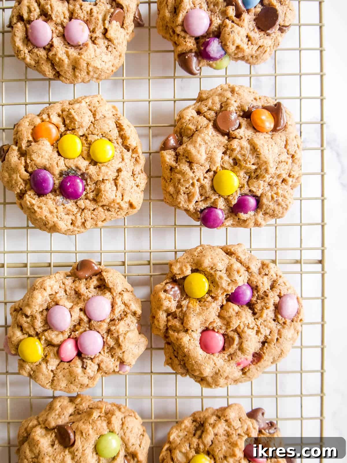 A fresh batch of gluten-free monster cookies cooling on a wire rack, perfectly baked with vibrant candies and melted chocolate.