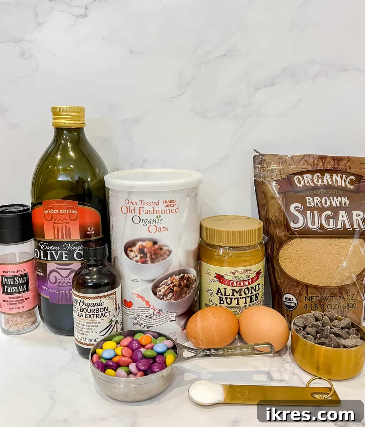 A selection of ingredients laid out, including oats, brown sugar, eggs, almond butter, and chocolate candies, ready for baking almond butter flourless monster cookies.