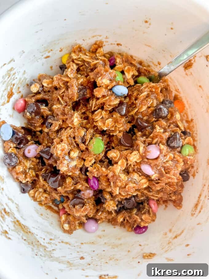 Chocolate chips and chocolate candies being gently folded into the monster cookie batter, ensuring even distribution.