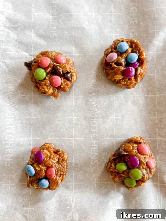 Unbaked no-flour monster cookies, perfectly scooped and topped with extra chocolate candies on a parchment-lined cookie sheet.
