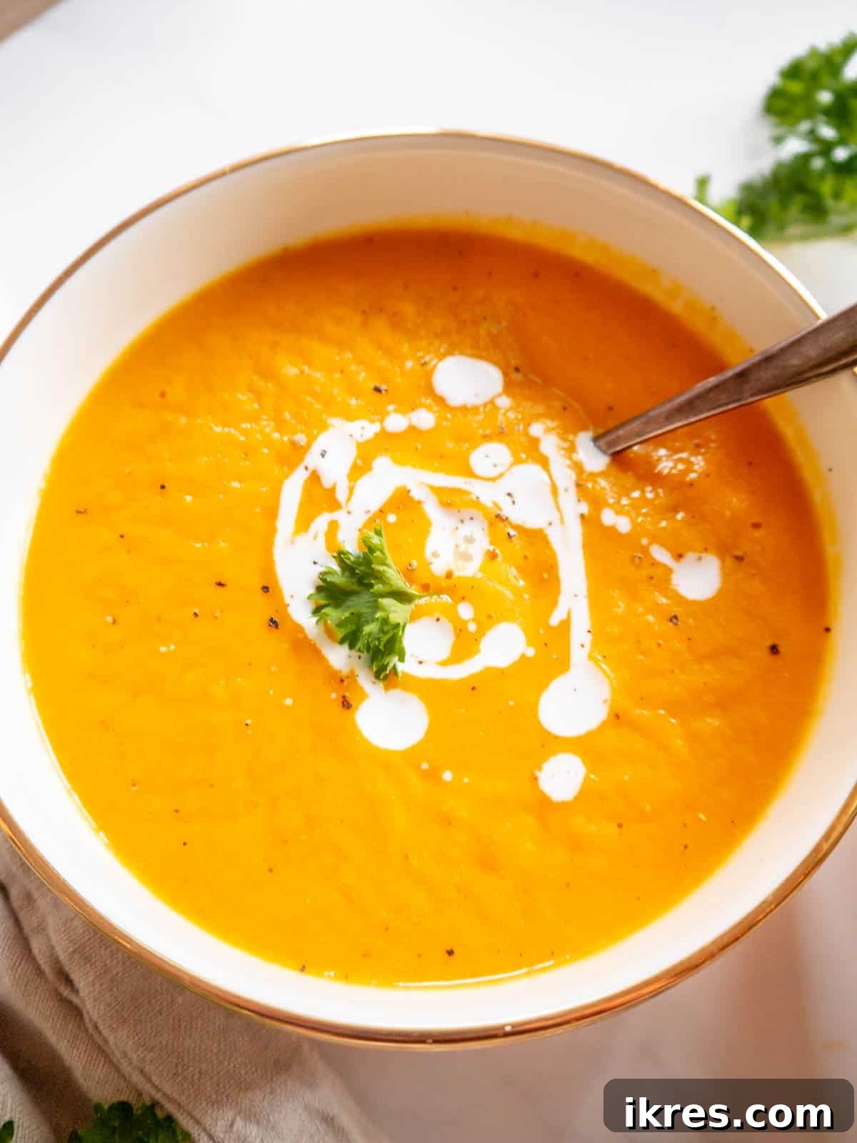 Velvety Butternut Squash and Carrot Soup 2 Butternut squash carrot ginger soup in a bowl with cream drizzled on top, garnished with fresh herbs.