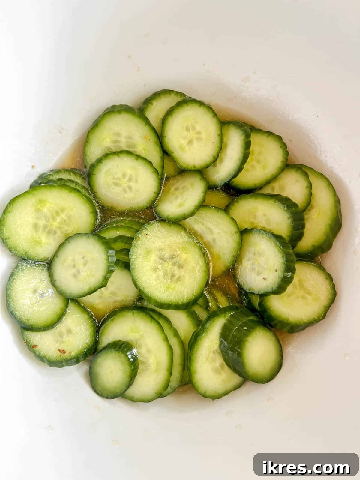 Crisp Asian Quick Pickles 5 The pickling brine, a mixture of apple cider vinegar, maple syrup, water, sesame oil, salt, and pepper, being poured over the sliced cucumbers.