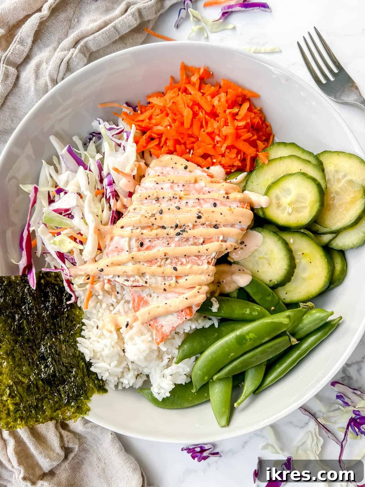 An assembled spicy salmon rice bowl on a plate, featuring salmon, rice, vegetables, and spicy mayo.