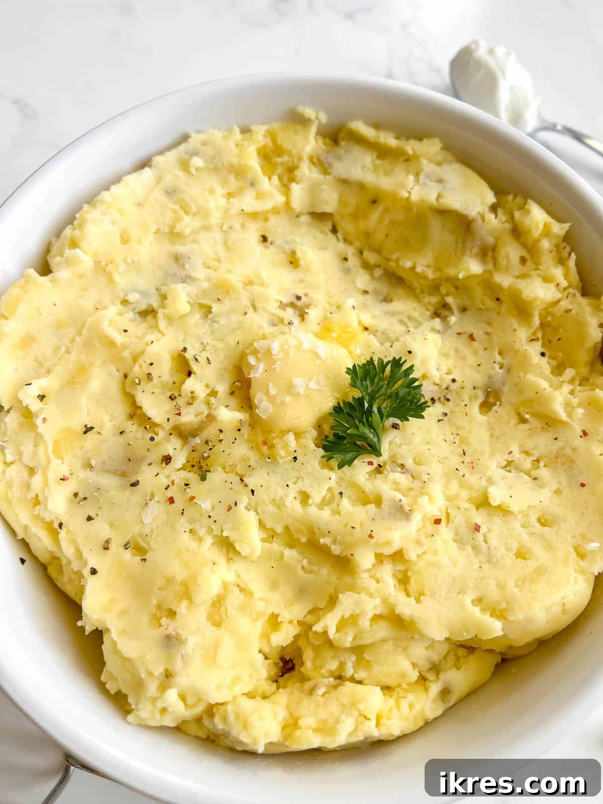 Greek yogurt mashed potatoes in a large bowl with butter melting on top, garnished with fresh herbs.