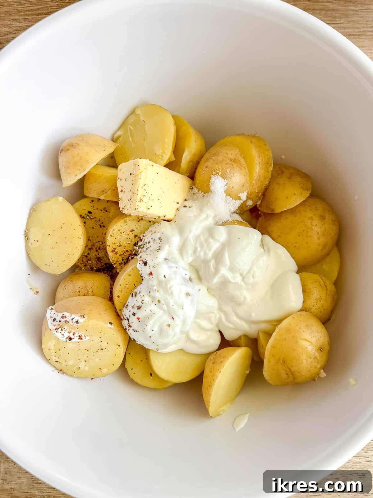 Drained boiled potatoes in a bowl, with Greek yogurt, butter, milk, salt, and pepper added on top, ready for mashing.