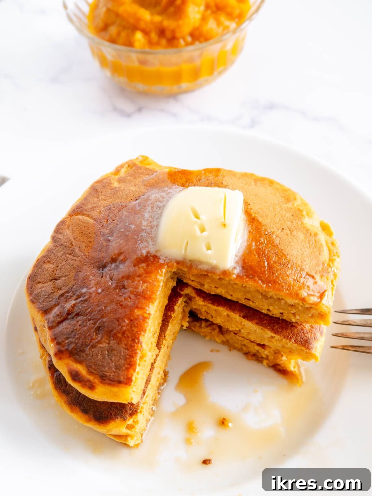 A tall, enticing stack of healthy pumpkin Greek yogurt pancakes, generously drizzled with maple syrup and ready to be enjoyed.