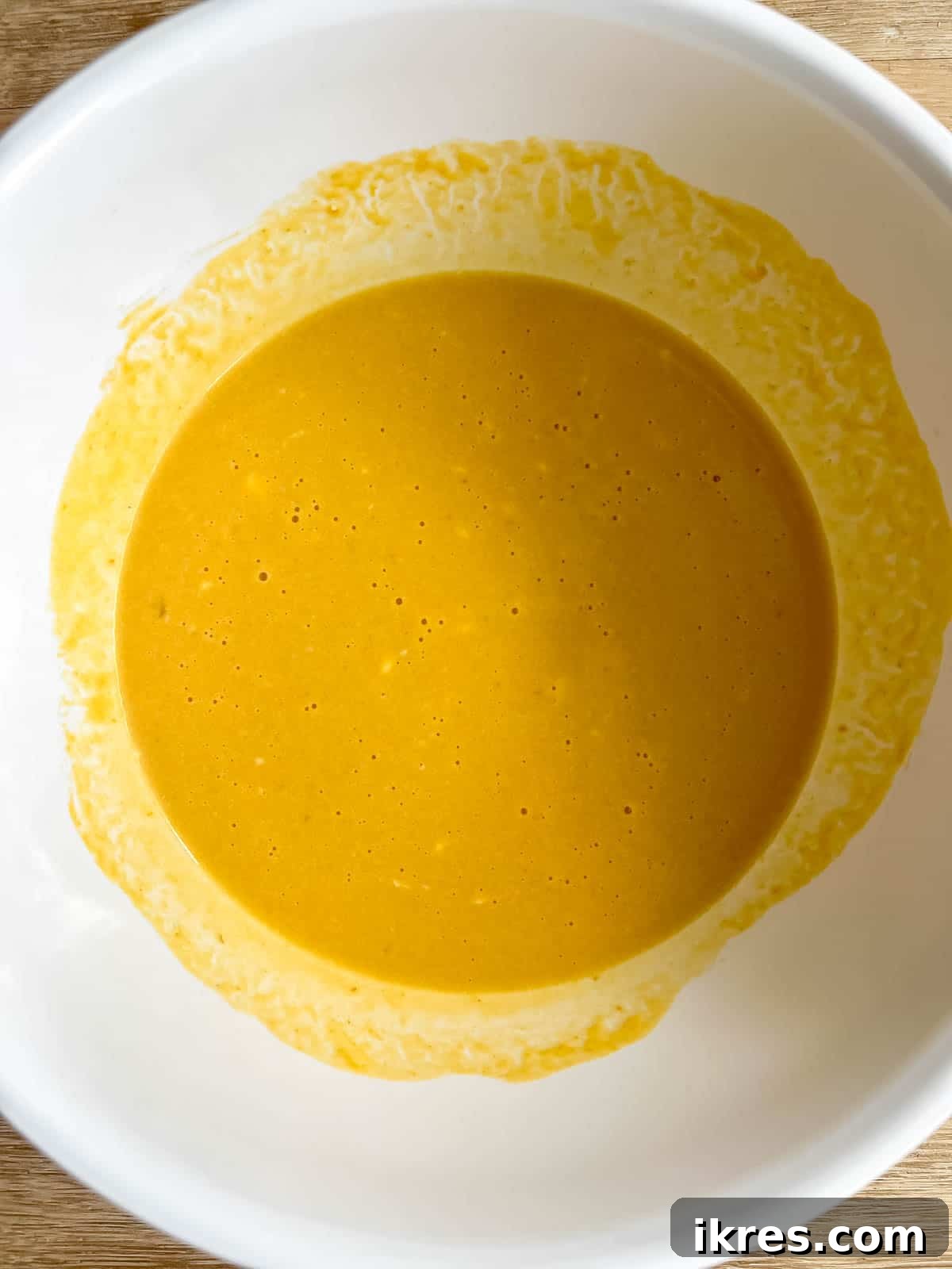 Wet ingredients for pumpkin pancakes (eggs, Greek yogurt, pumpkin puree, maple syrup) being whisked together in a bowl.