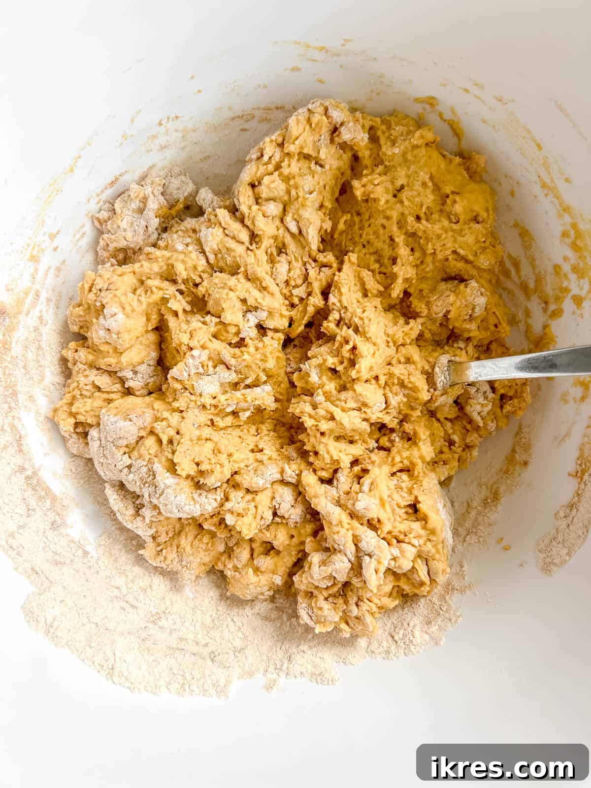 The bowl of dry ingredients being poured into the bowl of wet ingredients, showing a thick pumpkin pancake batter forming.