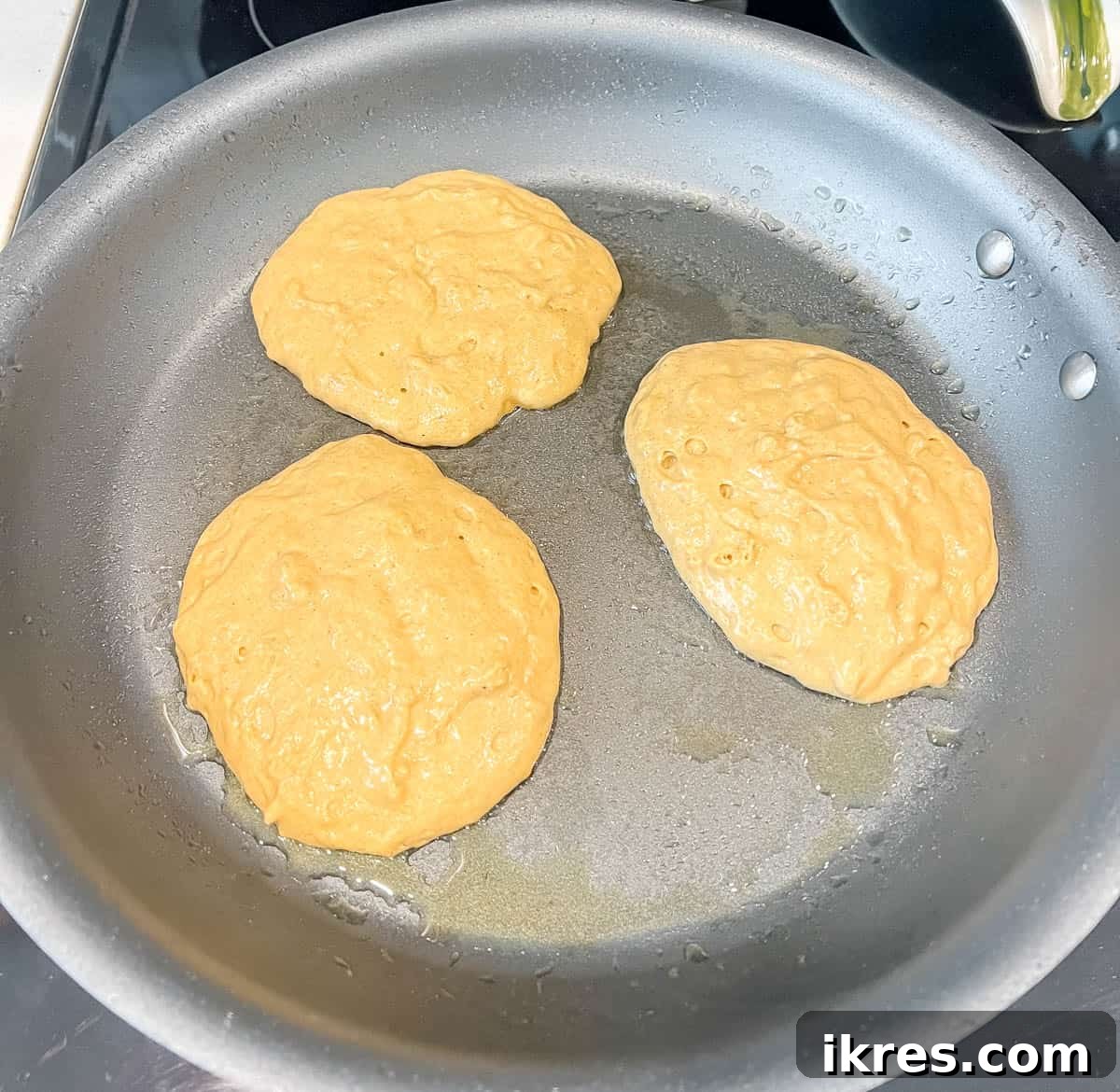 Healthy pumpkin pancakes cooking on a hot griddle, showing the batter spreading out.