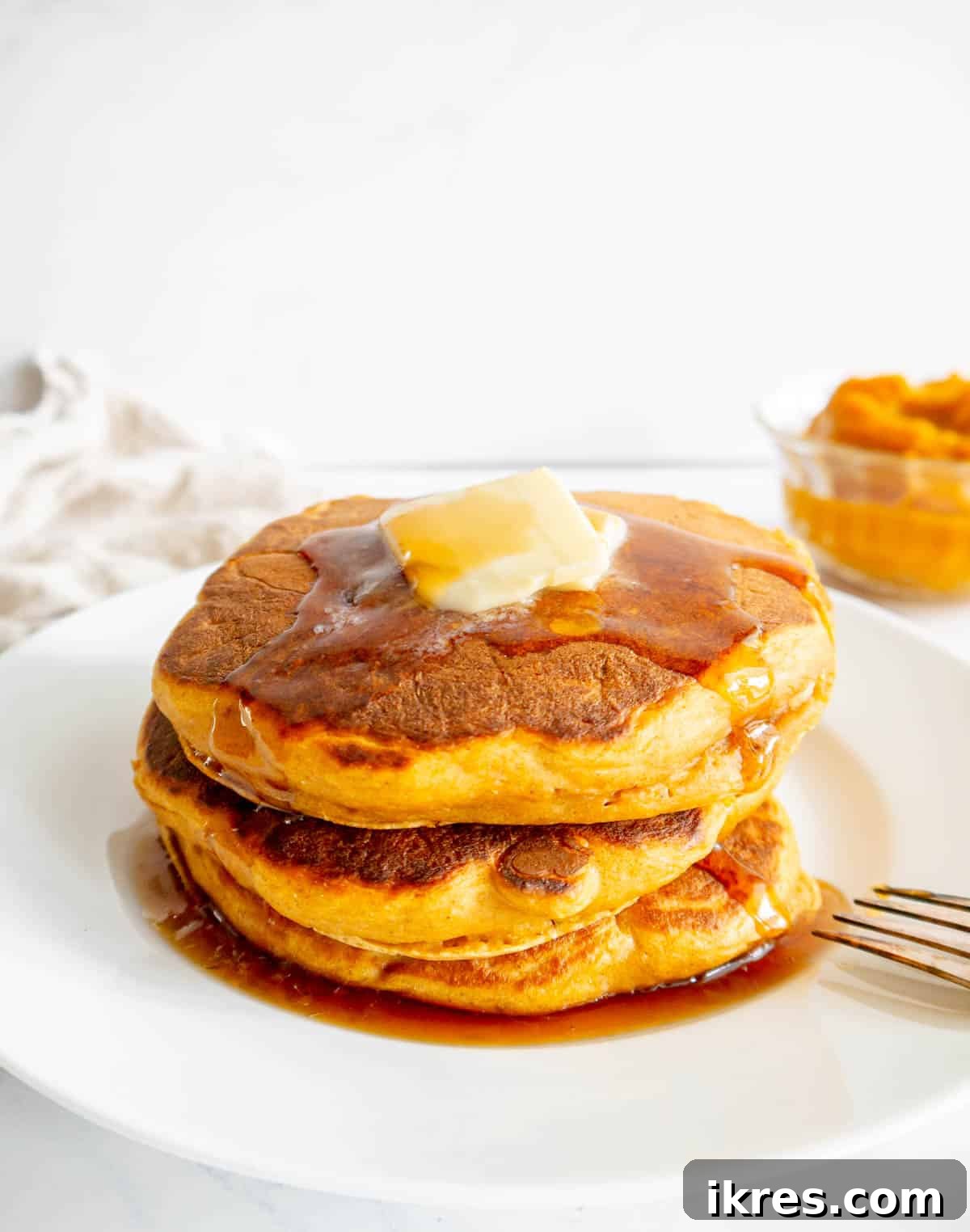 A plate of healthy pumpkin pancakes served with a pat of butter and a generous drizzle of maple syrup.