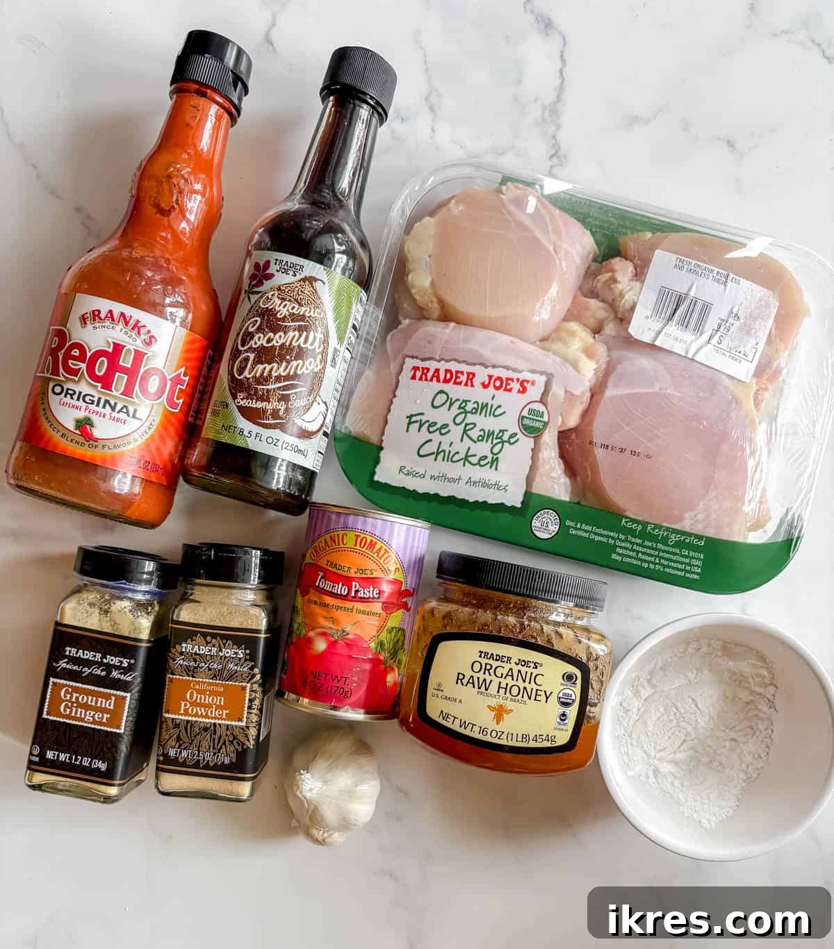Individual ingredients neatly arranged, ready to make slow cooker honey garlic chicken: chicken breasts, coconut aminos, honey, tomato paste, onion powder, ground ginger, hot sauce, fresh garlic, and tapioca flour.