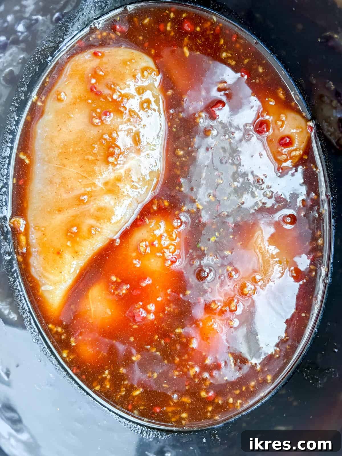 Raw chicken breasts submerged in a honey garlic sauce within a slow cooker, before cooking.