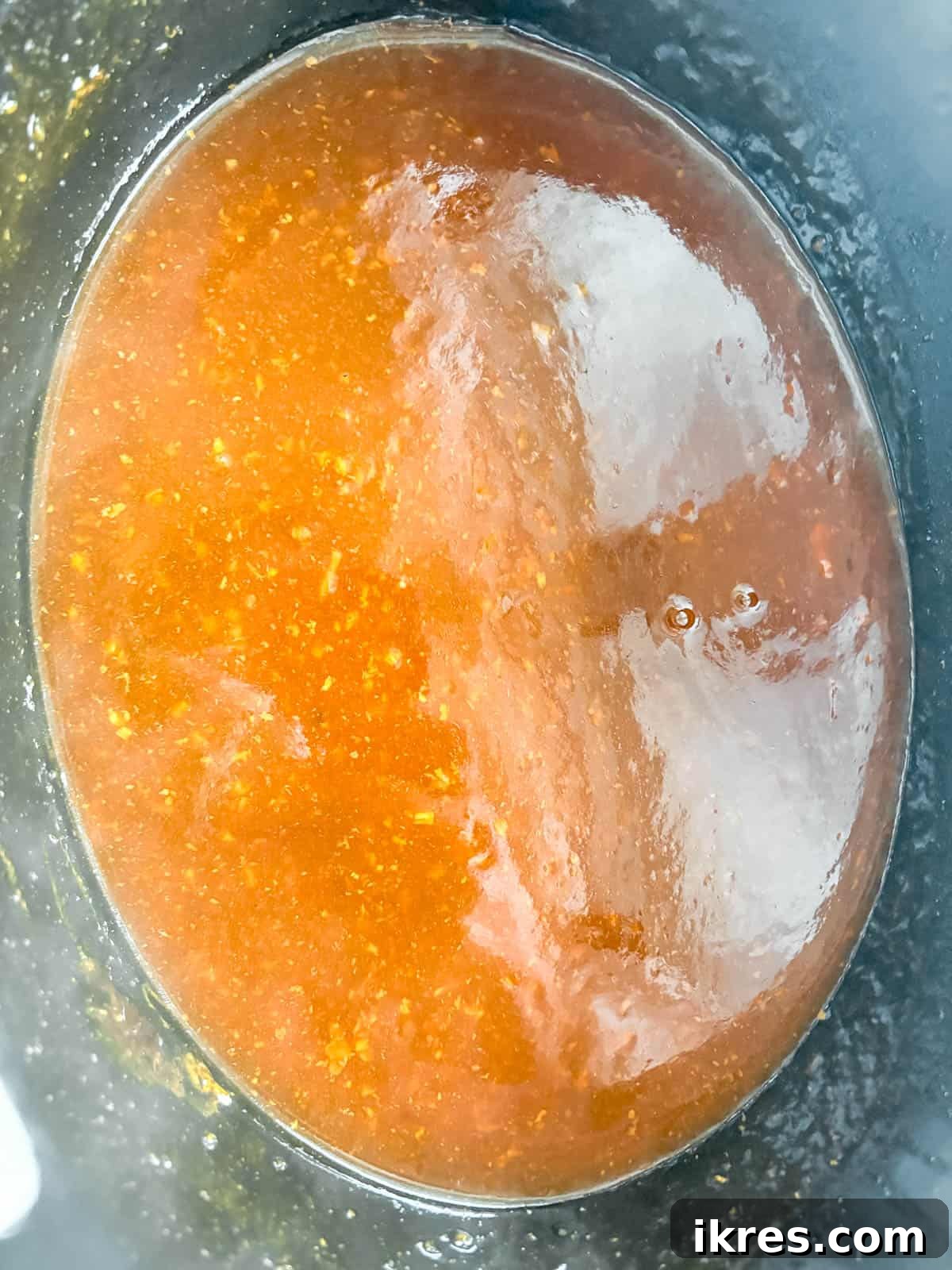 The honey garlic sauce in the slow cooker bubbling and thickening after the slurry has been added.