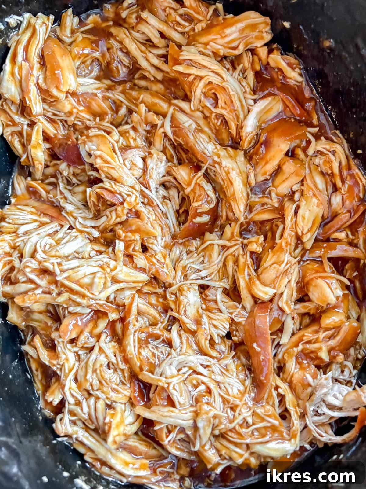 Shredded honey garlic chicken mixed back into the thickened sauce in the slow cooker.