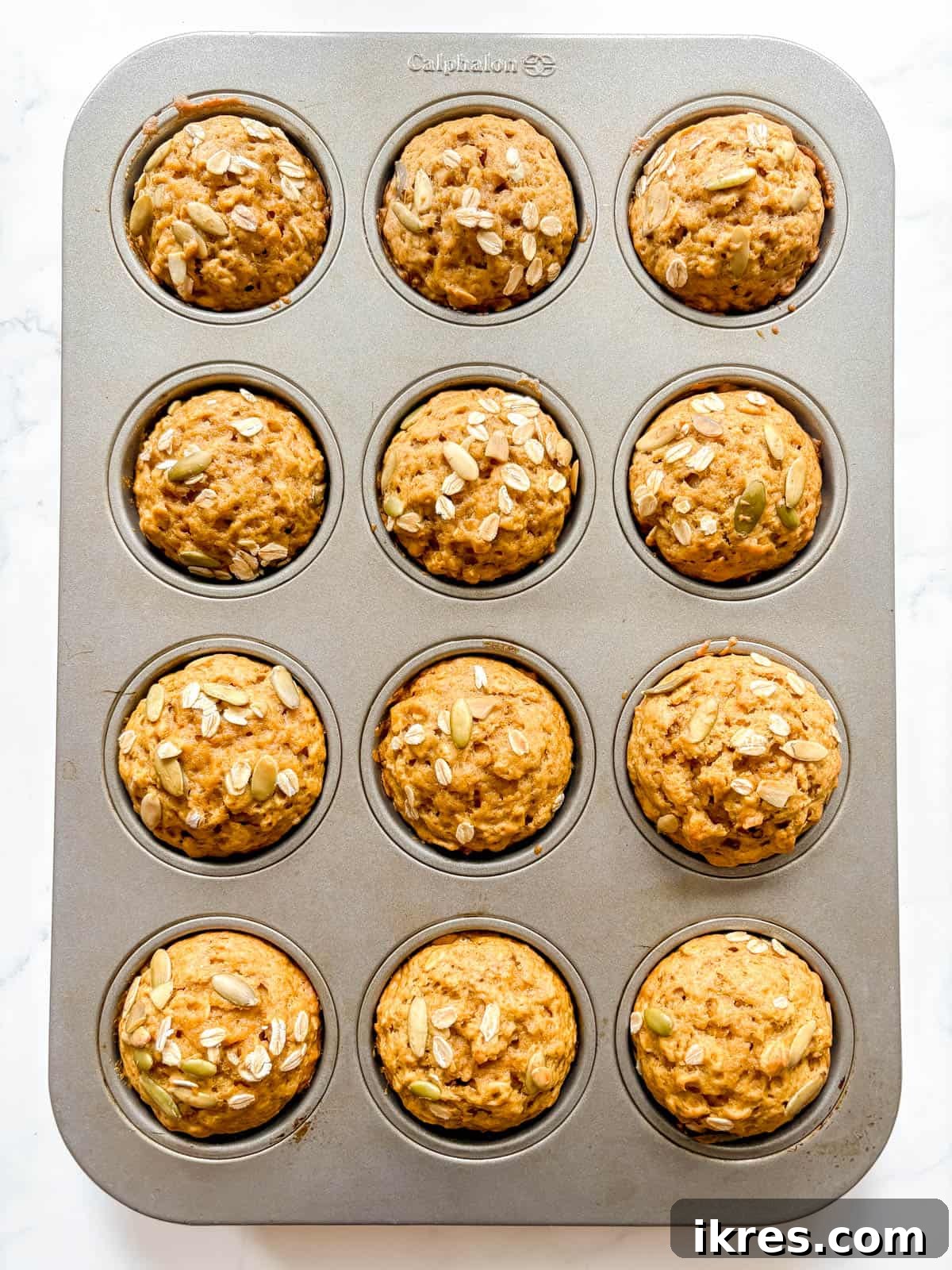 Plant-Based Pumpkin Spice Oat Muffins 8 Freshly baked pumpkin oatmeal muffins, golden brown and puffed, cooling in a muffin tin.