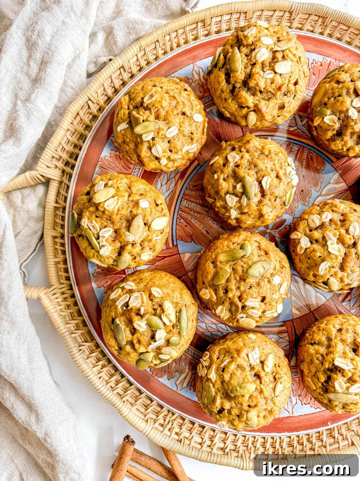 Plant-Based Pumpkin Spice Oat Muffins 9 A trio of dairy-free pumpkin oat muffins on a rustic white plate, garnished with rolled oats and pumpkin seeds on top.
