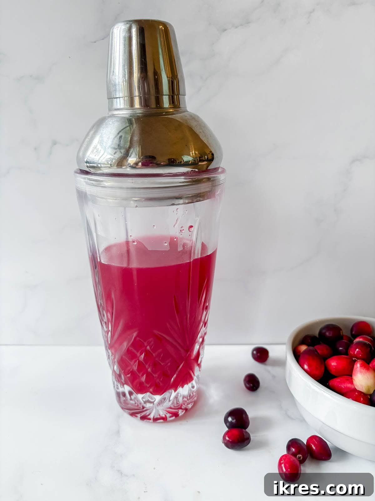 All cranberry margarita ingredients (tequila, Cointreau, lime juice, cranberry juice, maple syrup) poured into a cocktail shaker.