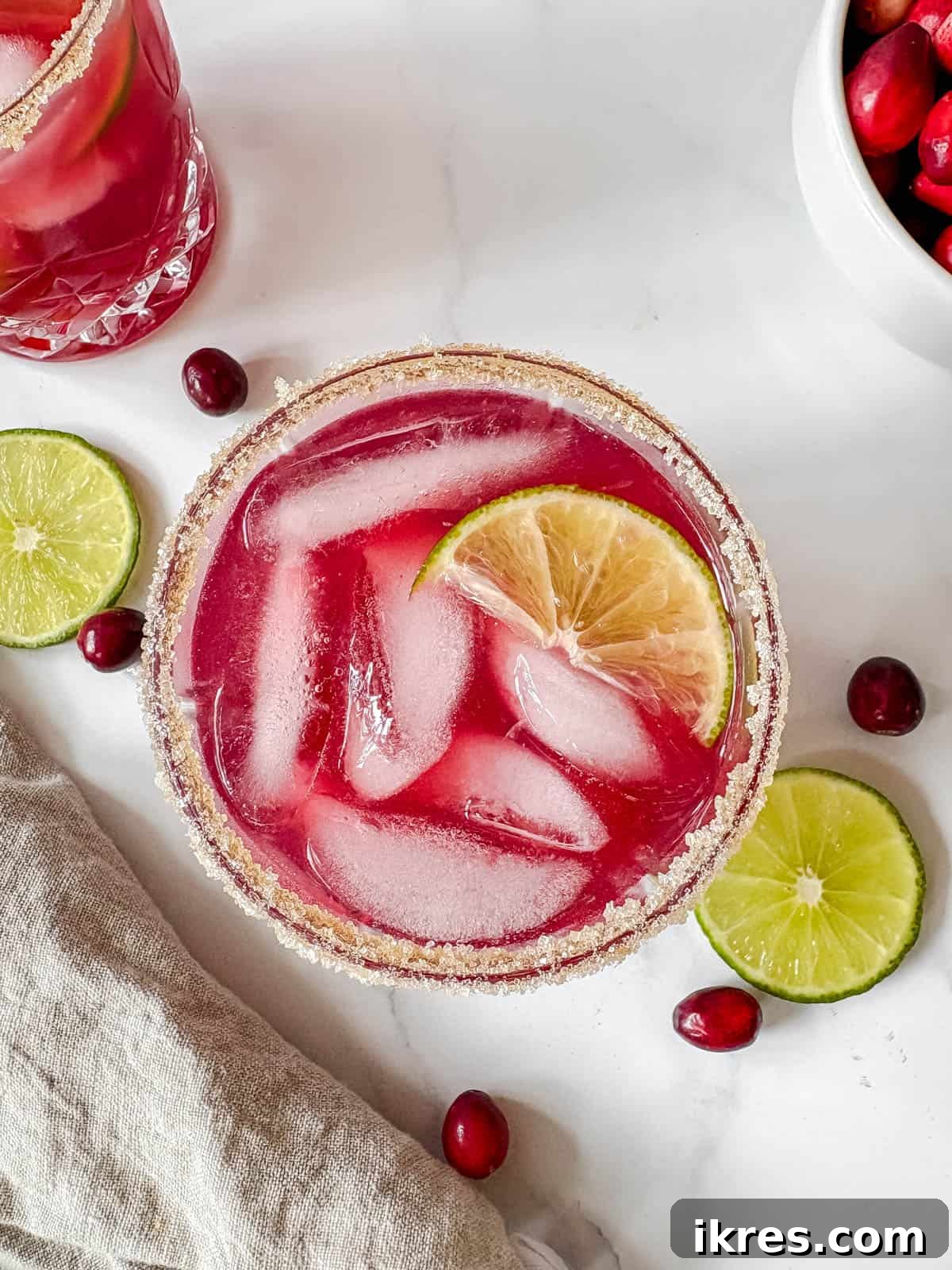 Finished cranberry lime margarita in a sugar-rimmed glass with ice and a lime slice garnish.