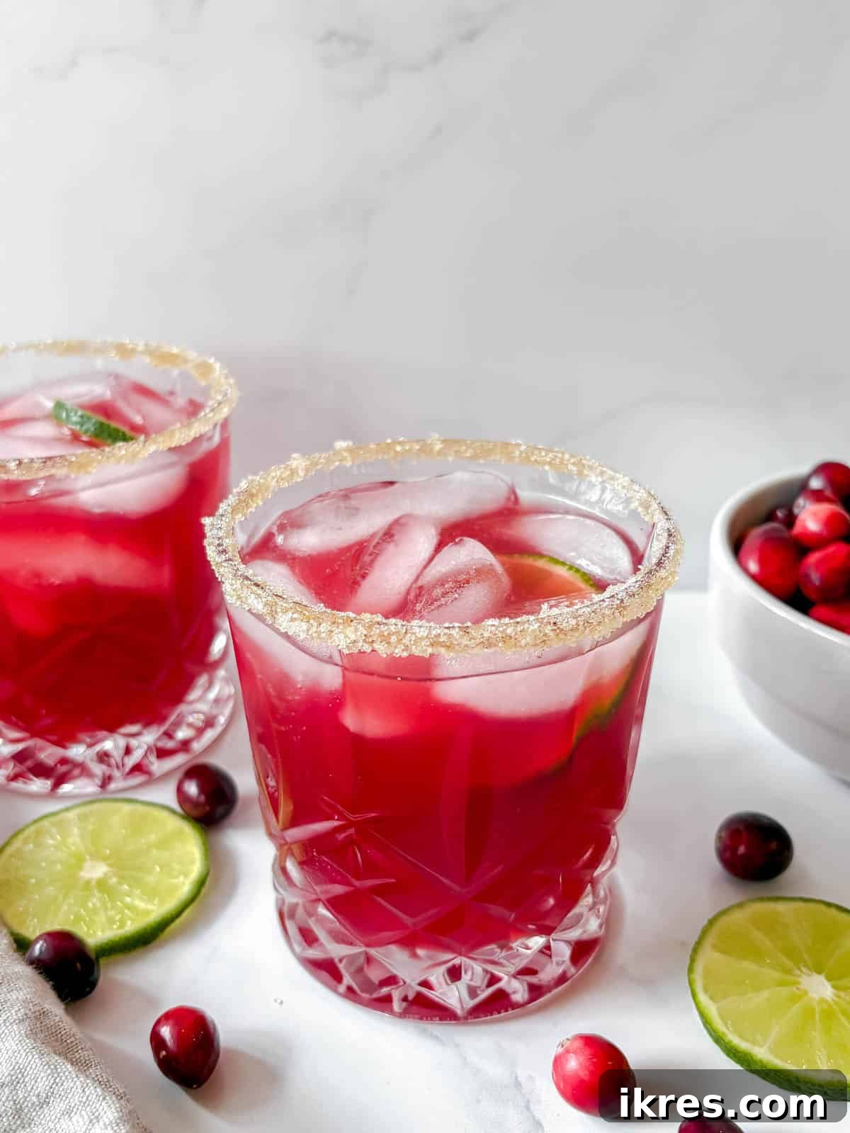 Cranberry margarita in a glass, surrounded by fresh cranberries and a lime slice on a festive background.