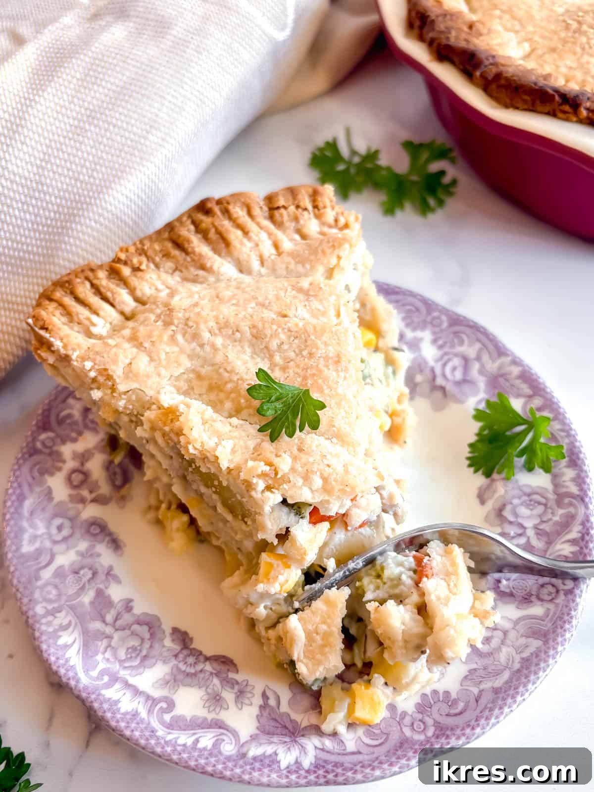 A fork is gently pressed into a slice of double-crust chicken pot pie, highlighting its flaky texture.