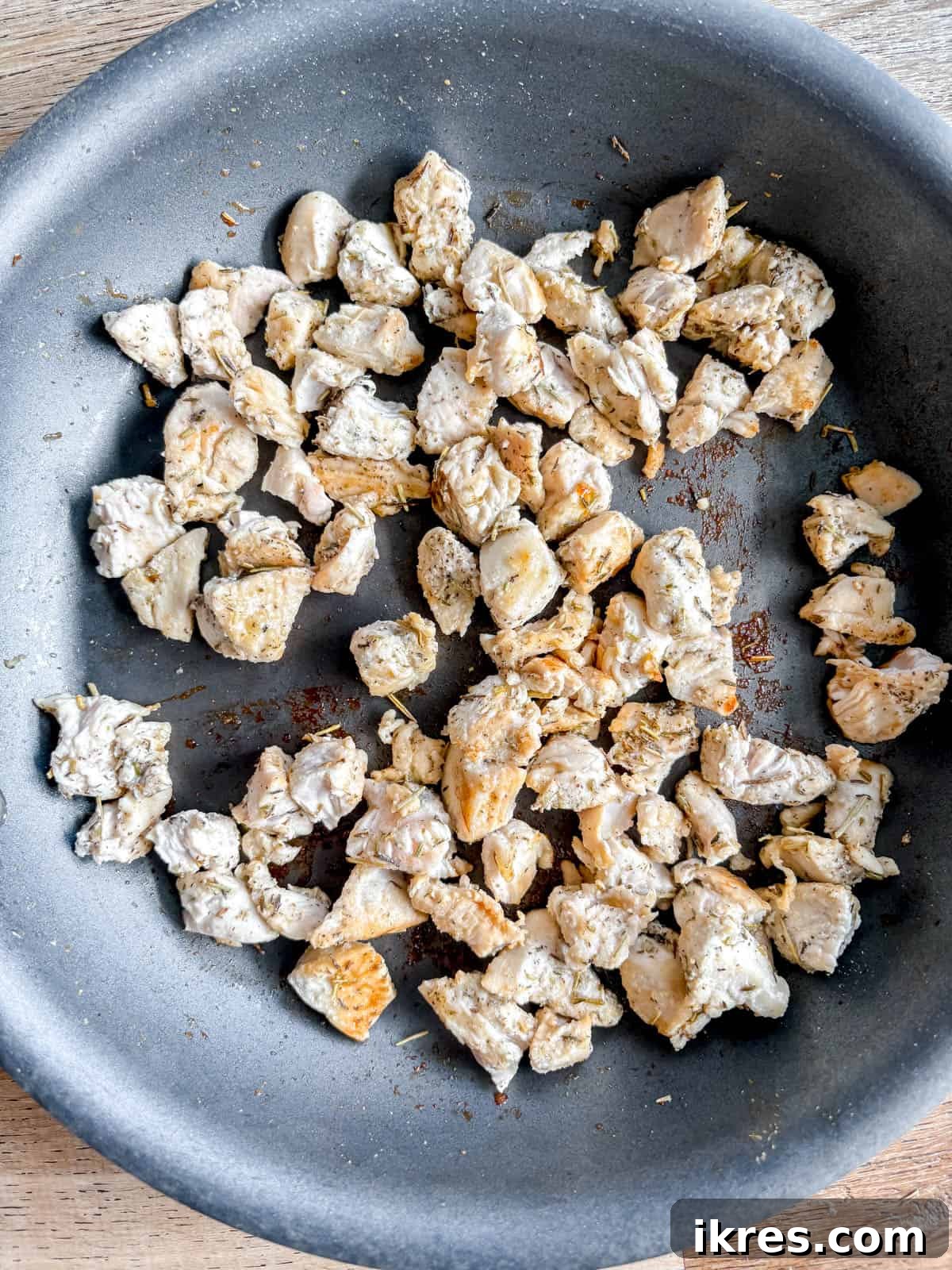 Bite-sized chicken pieces cooking in a pan with herbs and spices.