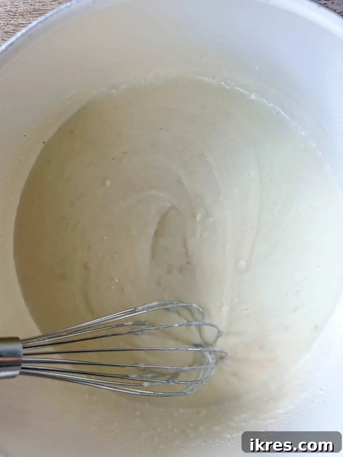 Milk being gradually added to the butter and flour mixture, whisking to form a smooth sauce.