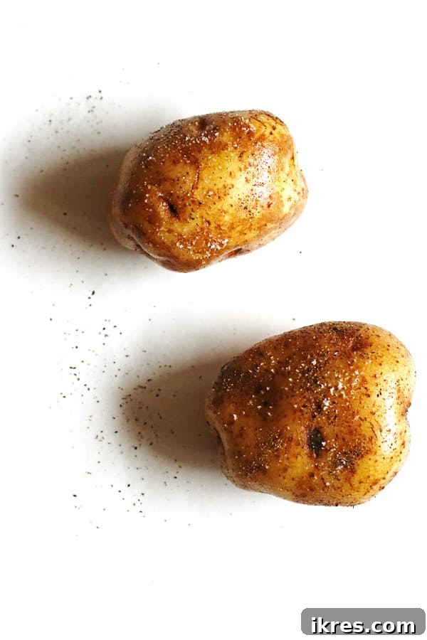 Ultimate Crispy Cheesy Bacon Potato Skins 3 Raw Russet potatoes, generously rubbed with olive oil and sprinkled with salt and pepper, resting on a clean white kitchen counter, prepped for baking.