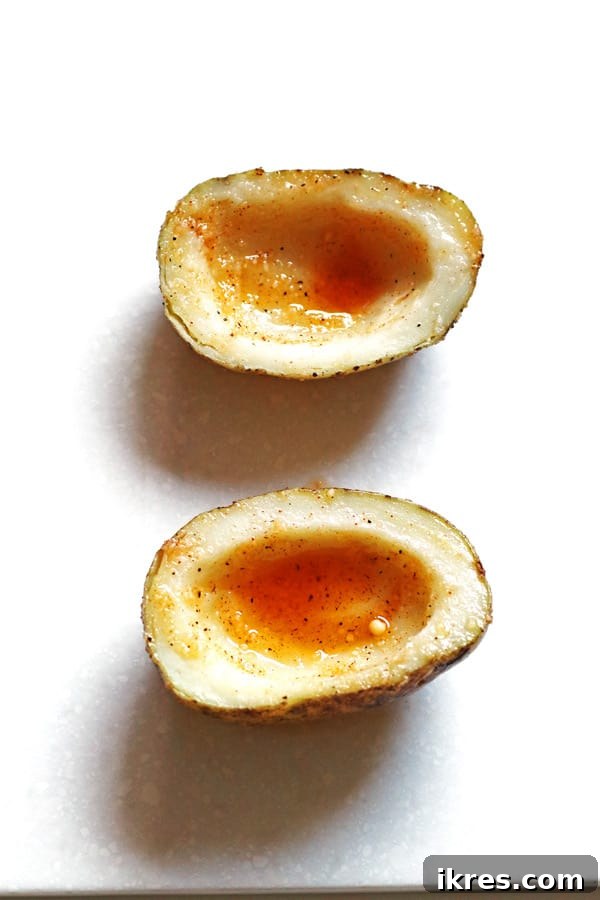 Ultimate Crispy Cheesy Bacon Potato Skins 5 Prepared potato skins, cut in half, scooped out, and evenly coated with a savory seasoning mixture, arranged on a baking sheet, ready for the oven.