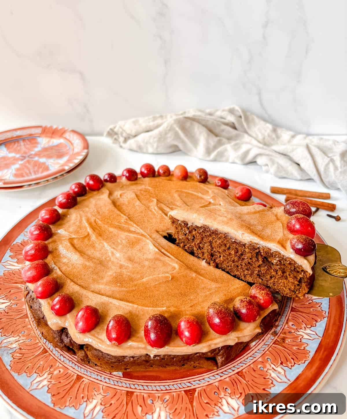 Spiced Gingerbread Cake with Tangy Cinnamon Cream Cheese Frosting 3 A slice of gingerbread cake with cream cheese frosting being served on a white plate with a gold fork.